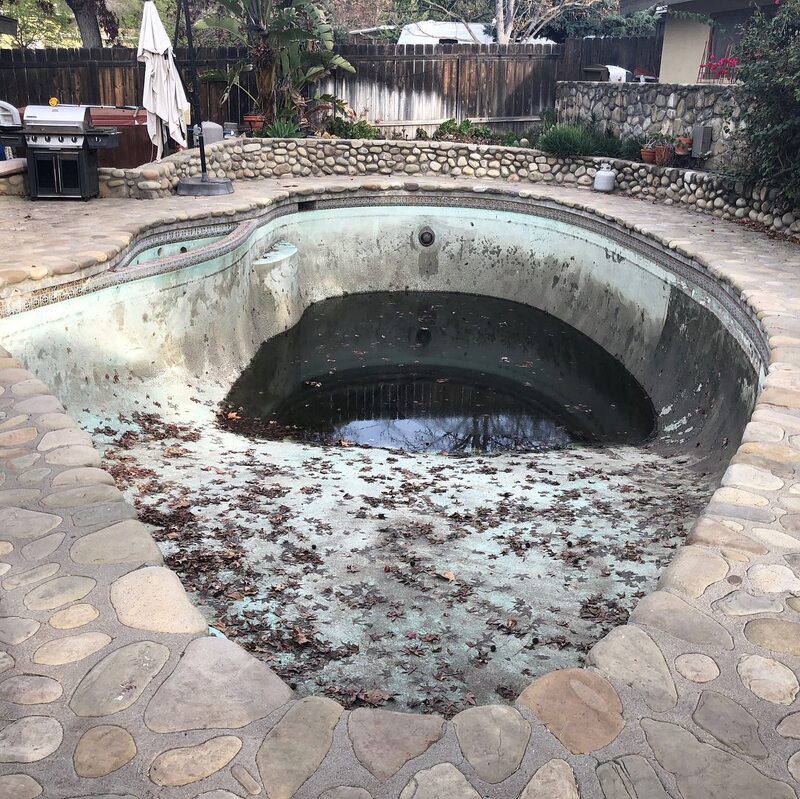 Drained pool before resurfacing, with a failed surface and debris
